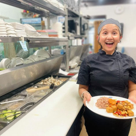 Rotchana Sussman standing with a plate of food in her hand with big smile into camera.