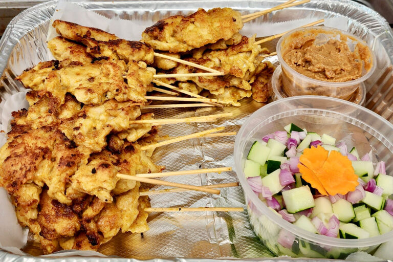 Party tray of chicken satay on sticks with sauce.